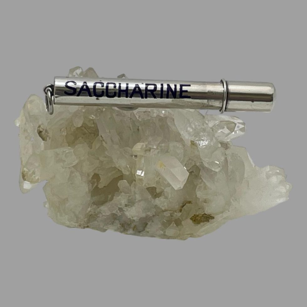 Main photo of antique silver saccharine tube displayed on top of a rock of natural quartz crystal with the enamelled blue 'Saccharine' written along the side on display. The opening end is on the right and is a simple pull off push on lid however it is very secure and tight. The opposite end has a ring clasp for attaching to keyrings or handbag zip or even on a silver chain to wear around the neck.