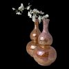 Main photo of gourd lustre ware vases displayed with one in front of the other and to the right so half of one behind is showing. The vase in the foreground is a slightly pinker shade than the one behind which is a little more orange. Both vases are the same shape. The pinker vase in the foreground has a spray of white orchids displayed from it. The black background enhances the beautiful lustre of the vases.