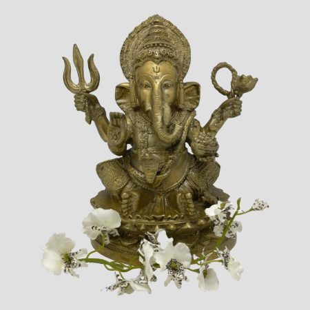 Main photo of antique bronze Lord Ganesha shown against a light grey background and facing forward at the camera. There a spray of white orchids laid around his feet. This bronze has a golden hue and is very well presented.