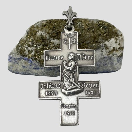 Main photo of French Joan of Arc cross seen with the side of Joan of Arc knelt in prayer in profile on show. The cross is leaning against a rock of lapis with the gold fleck side showing. The bail rests on top of the rock.