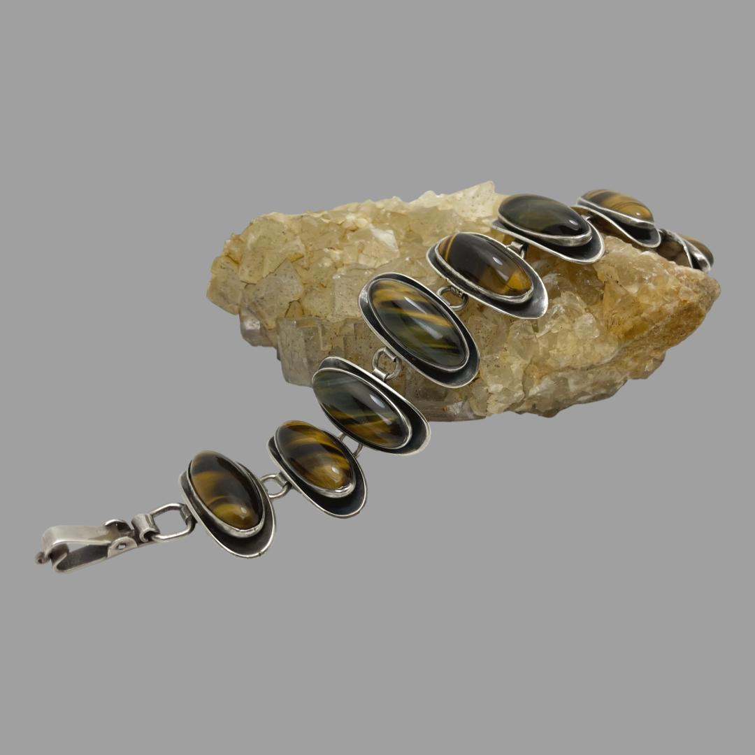 Main photo of tigers eye panel bracelet displayed spread over a rock of natural river quartz. The quartz is a light brown/beige colour which compliments this bracelets colours. This bracelet has a unique design with convex panels as the base with the tigers eye pieces added. There are 8 panels each connected together with a sturdy solid silver loop. The clasp is also nice and sturdy and is the fold over variety.