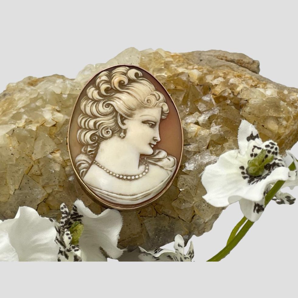 Main photo of antique 9kt gold cameo. The cameo is displayed balanced on a rock of natural river quartz which is a light brown/beige colour which compliments the colour of the cameo which is a pale terracotta background with creamy/beige profile of a lady. The carving of the lady is beautifully done. She has an exquisite serene look and is facing slightly with head down as if averting the gaze of someone - very dreamy piece!