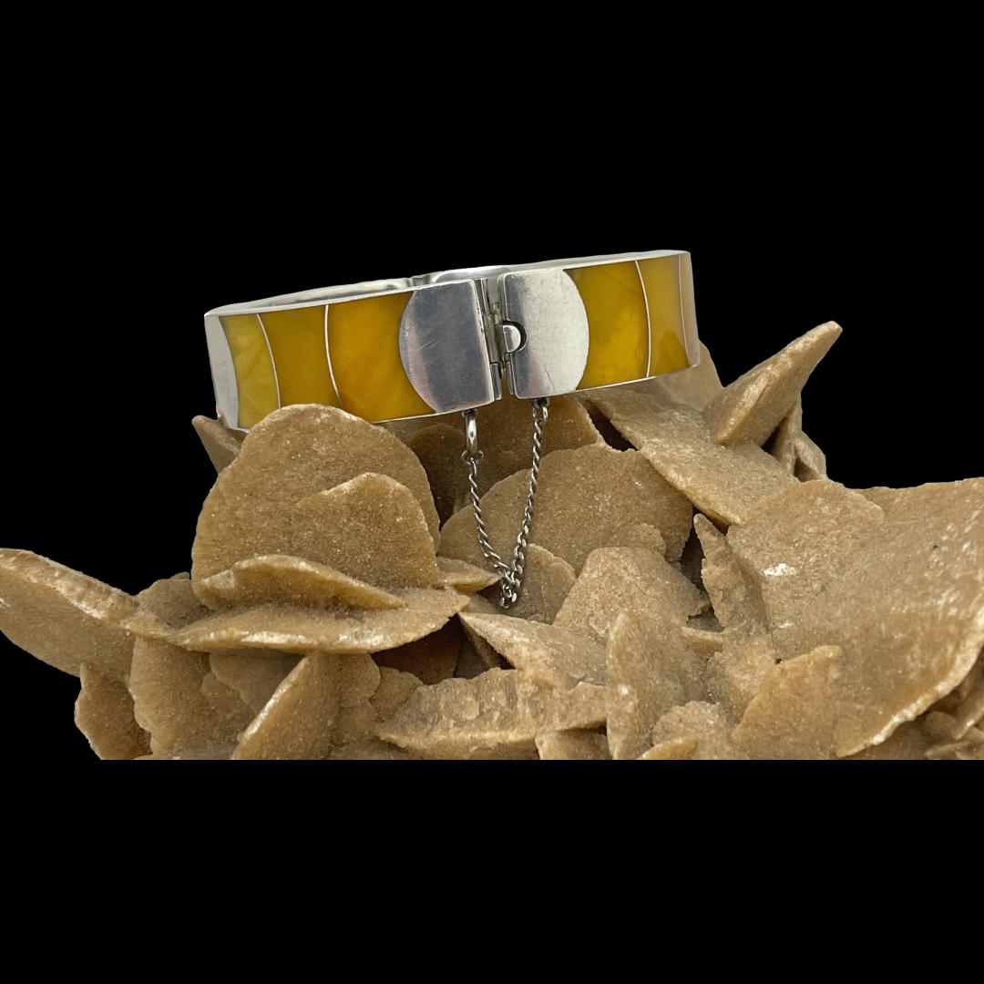Main photo of bracelet displayed on top of a rock of natural desert rose with the clasp section in the foreground. The amber pieces are in sections of different egg yolk amber shades which appear to be graduating in colour.