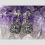 Main photo of deco style silver marcasite earrings displayed on a rock of natural amethyst crystal and shown forward facing. The top part of the earrings is line of silver with marcasite with square attached at ends housing a small square cut amethyst to centre of each within a frame of marcasite stones.