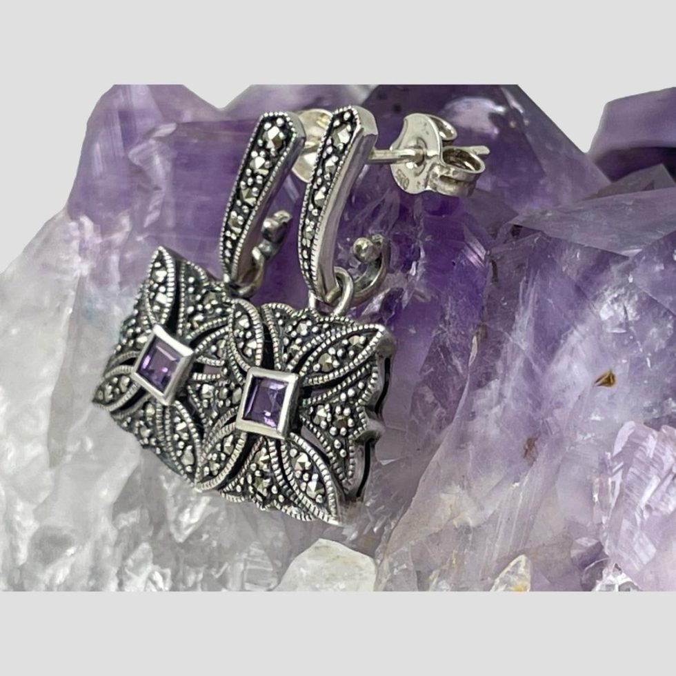 Photo of earrings still displayed hanging from a natural amethyst crystal rock with the earring fronts facing to the left.