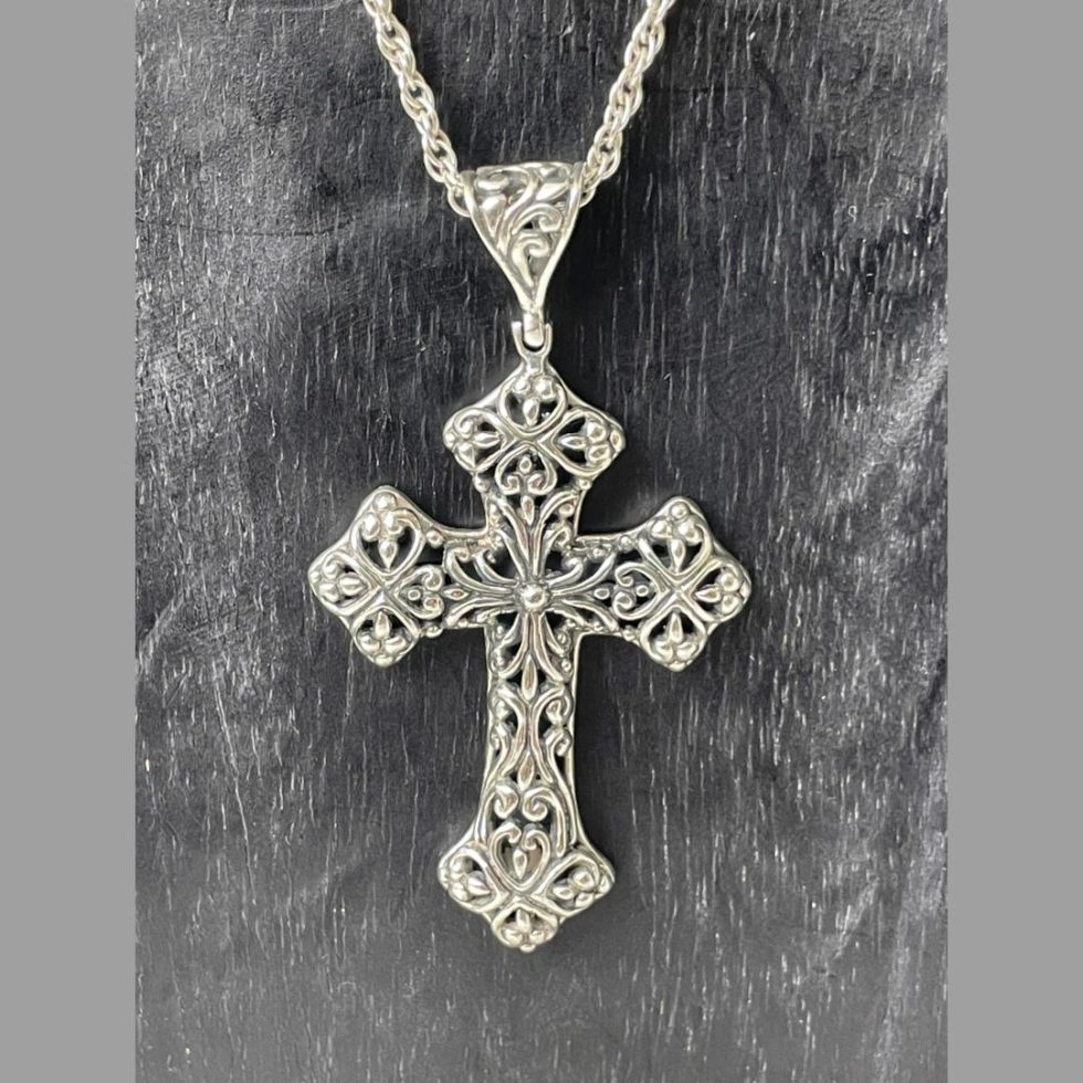 Photo of cross shown hanging from a display stand with just the cross area on display. The intricate pierced silver work side is on display.