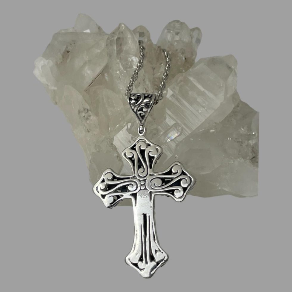 Photo of cross still leaning against a rock of natural quartz crystal and seen with the reverse side on display. Whilst not as intricate as other side, it is still very attractive with the added bonus of having the 925 hallmark on display!