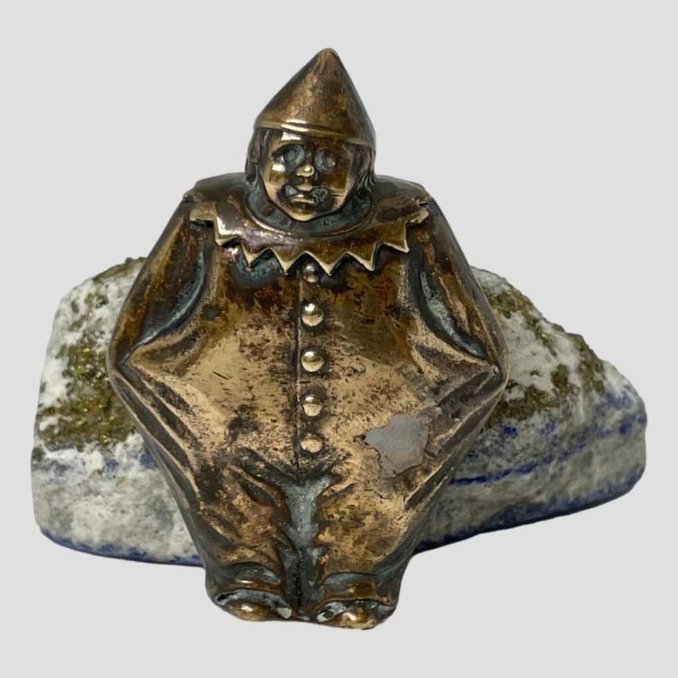 Main photo of antique brass clown vesta leaning against some natural lapis and seen forward facing.