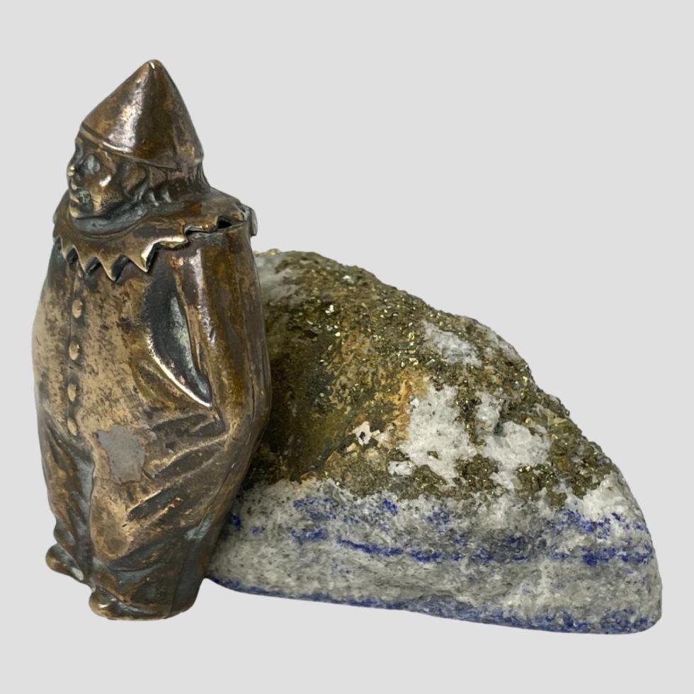 Photo of brass clown vesta still leaning on rock of lapis but from a slight side view.