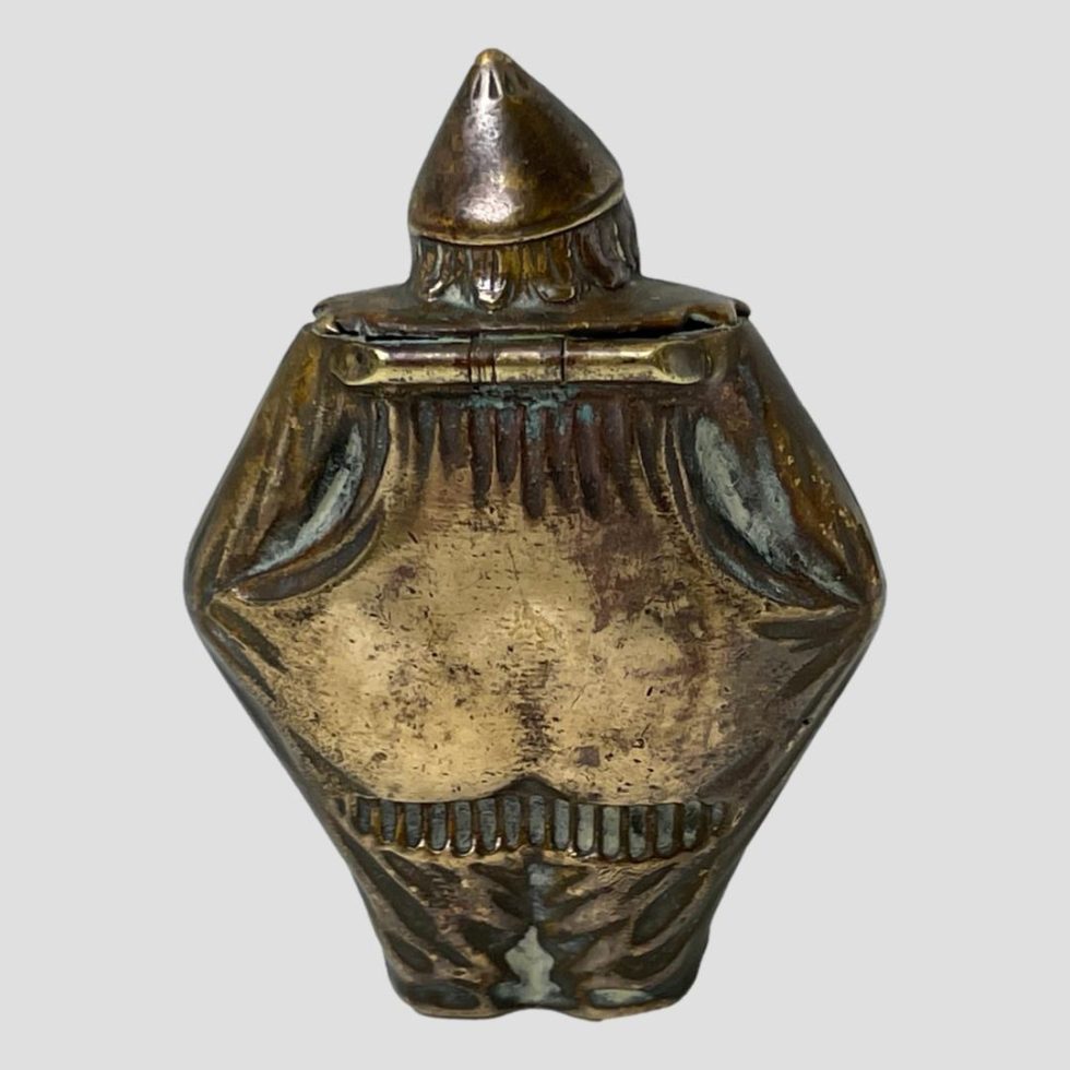 Photo of the back of the brass clown vesta showing the strike area below his buttocks.