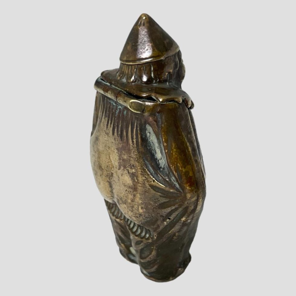 The brass clown vesta is shown facing away from camera and looking to the top right corner of photo. Looks a little as though skulking