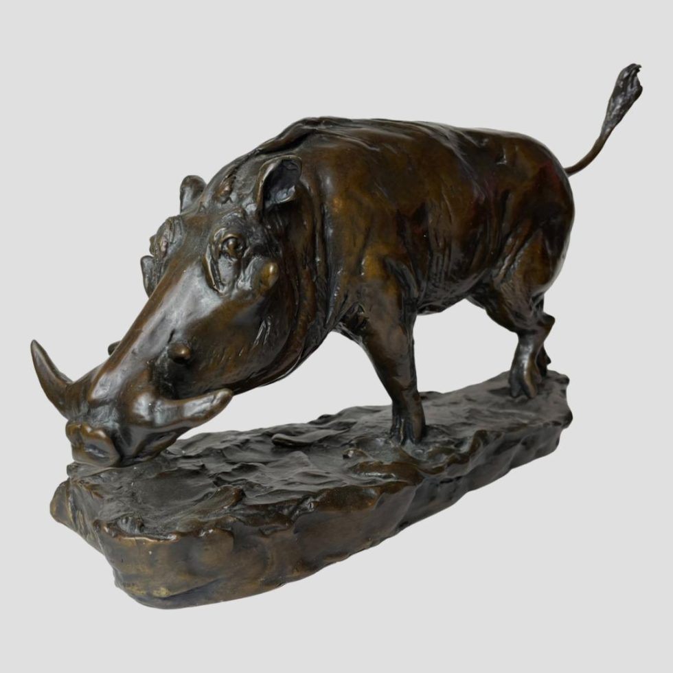 Main photo of wild boar bronze set at a diagonal angle with the head in the bottom left corner and tail pointed upward into the top right corner of photo. The boar has a long face with largish tusks and stood on an ununiform lump of bronze which looks like earth.
