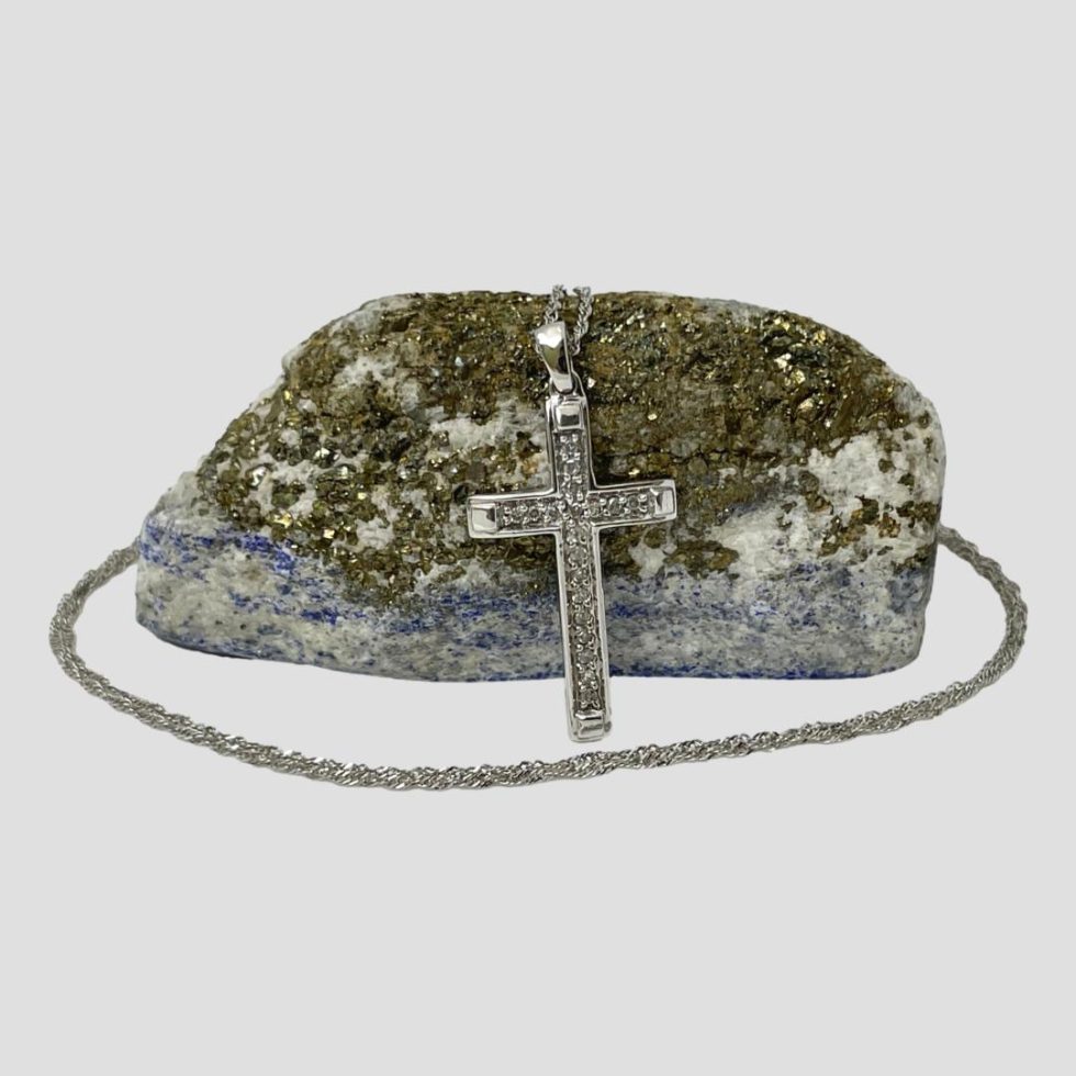 Main photo of gold diamond cross and chain shown with cross leaning against a rock of lapis with gold ore and seen forward facing. The chain extends over the top of rock of lapis and circles round the front.