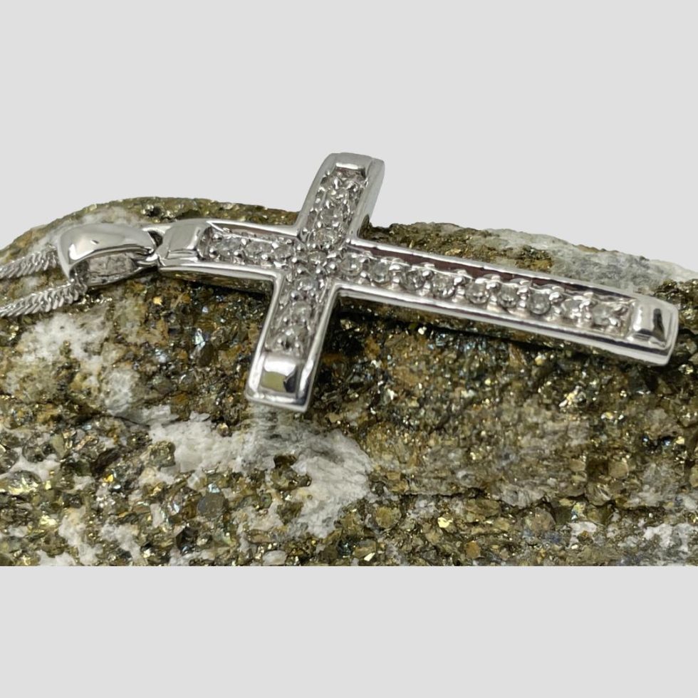 Photo of gold diamond cross displayed laid horizontally on top of gold ore rock. The bail end is to the left with part of the chain visible and the depth of the cross.