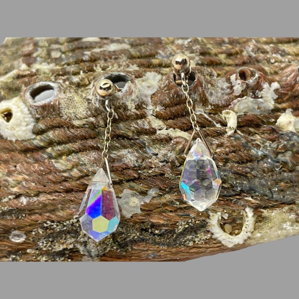 Another photo of aurora crystal earrings this time hanging from a shell. The earring on the left is reflecting amazing colours whilst the one on right is mostly clear with a few specks of colour visible. This photo shows how a change of light can affect the colours from the crystals.