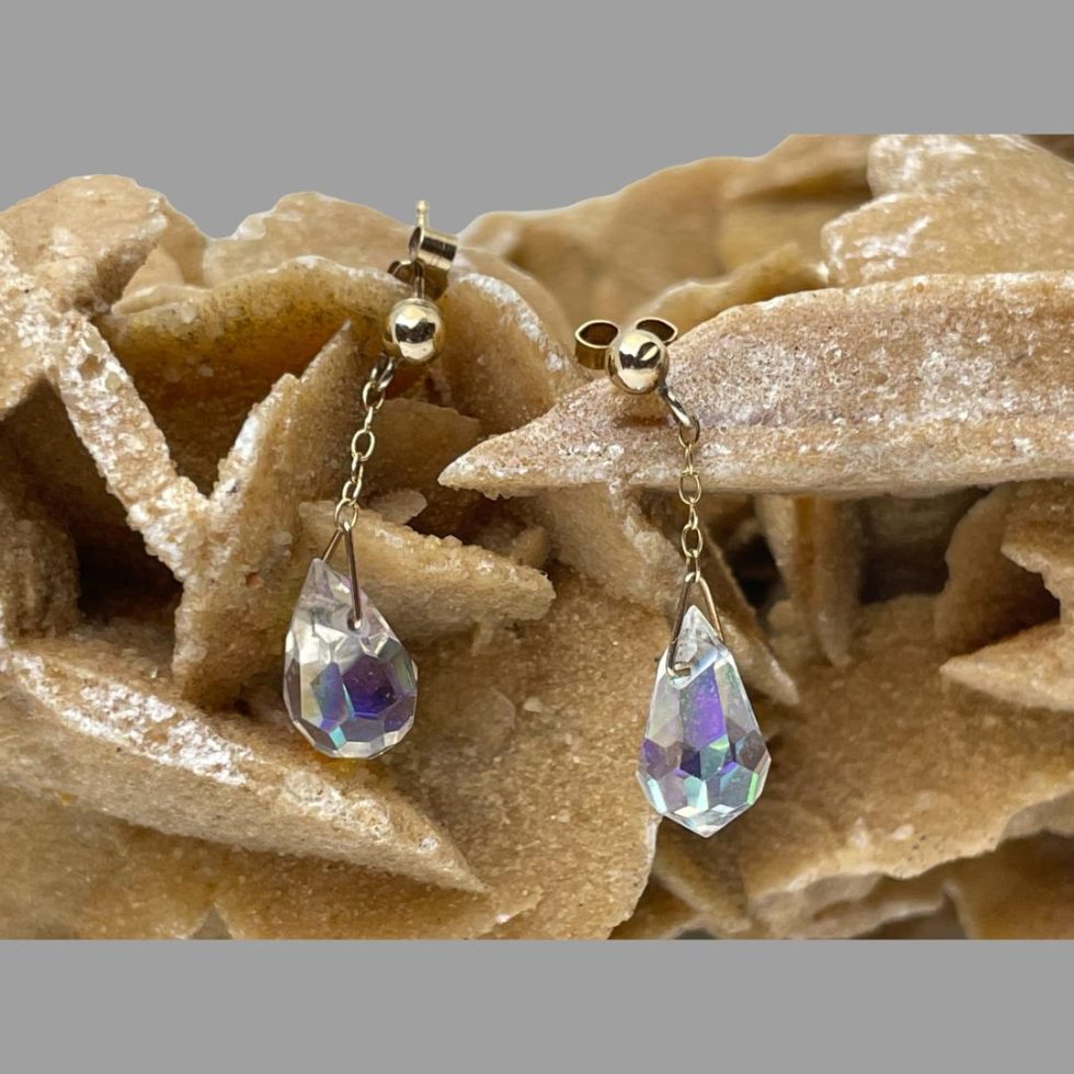Main photo of vintage aurora crystal earrings hanging balanced on a rock of natural desert rose. The colours of the crystals appear subtle here but there is evidence of a whole rainbow and more of colour waiting to shine out.