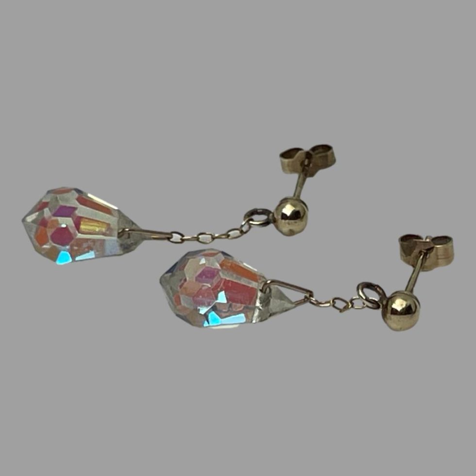 Photo of the earrings laid side by side horizontally on a flat surface with the post ends on the right. The light on the crystal drops are reflecting shades of turquoise pink peach and orange.