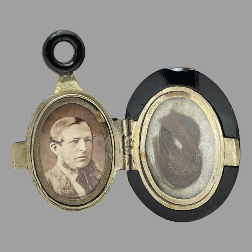 Photo of open Victorian jet locket shown open with the interior on display. To the left is the smaller section with photograph and on the right is the larger section housing the braided hair piece. Both sections have nice brass finish each framed in brass. This locket is all the more unusual in that it opens to the right and not left as most lockets.