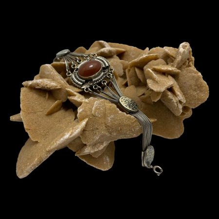 Main image of Indian silver carnelian bracelet draped over a rock of natural desert sand rose. One end of the bracelet is hanging off the side of the rock and the central area of bracelet with the carnelian cabochon is on top of the rock and facing upward towards top left corner.