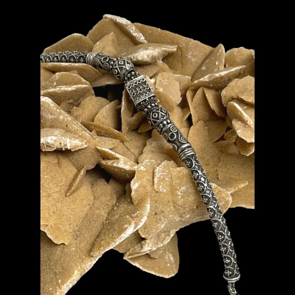 Photo of vintage Rajasthani silver necklace draped across a rock of natural desert sand rose and focusing on one half of necklace beads with the longest end tube bead in the foreground and the central square bead on the rocks top.