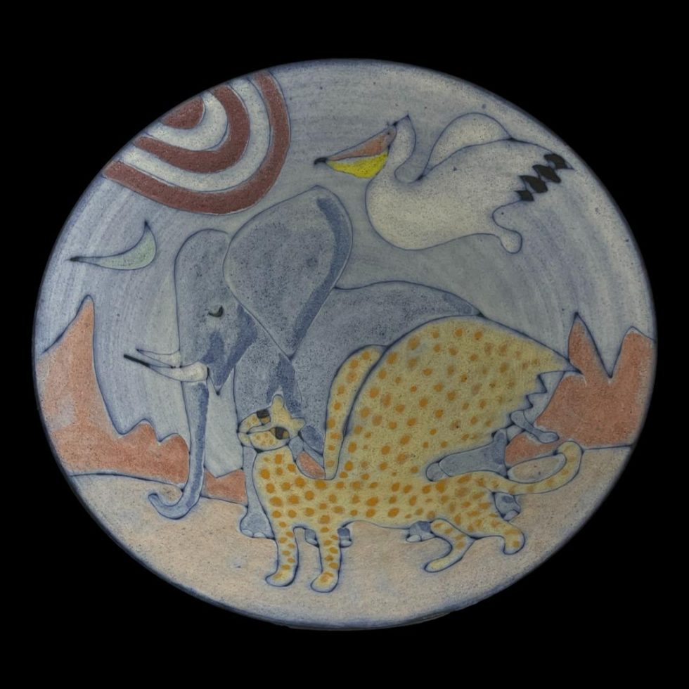 Main photo of Tessa Fuchs animals bowl showing the incredible art work in the bowl centre. The sun is to the top left with crescent moon just below it. The pelican in flight is just right of the sun, the elephant to the centre and the winged cheetah creature in the foreground and there is a red mountain range in the background. All creatures are facing and heading left.