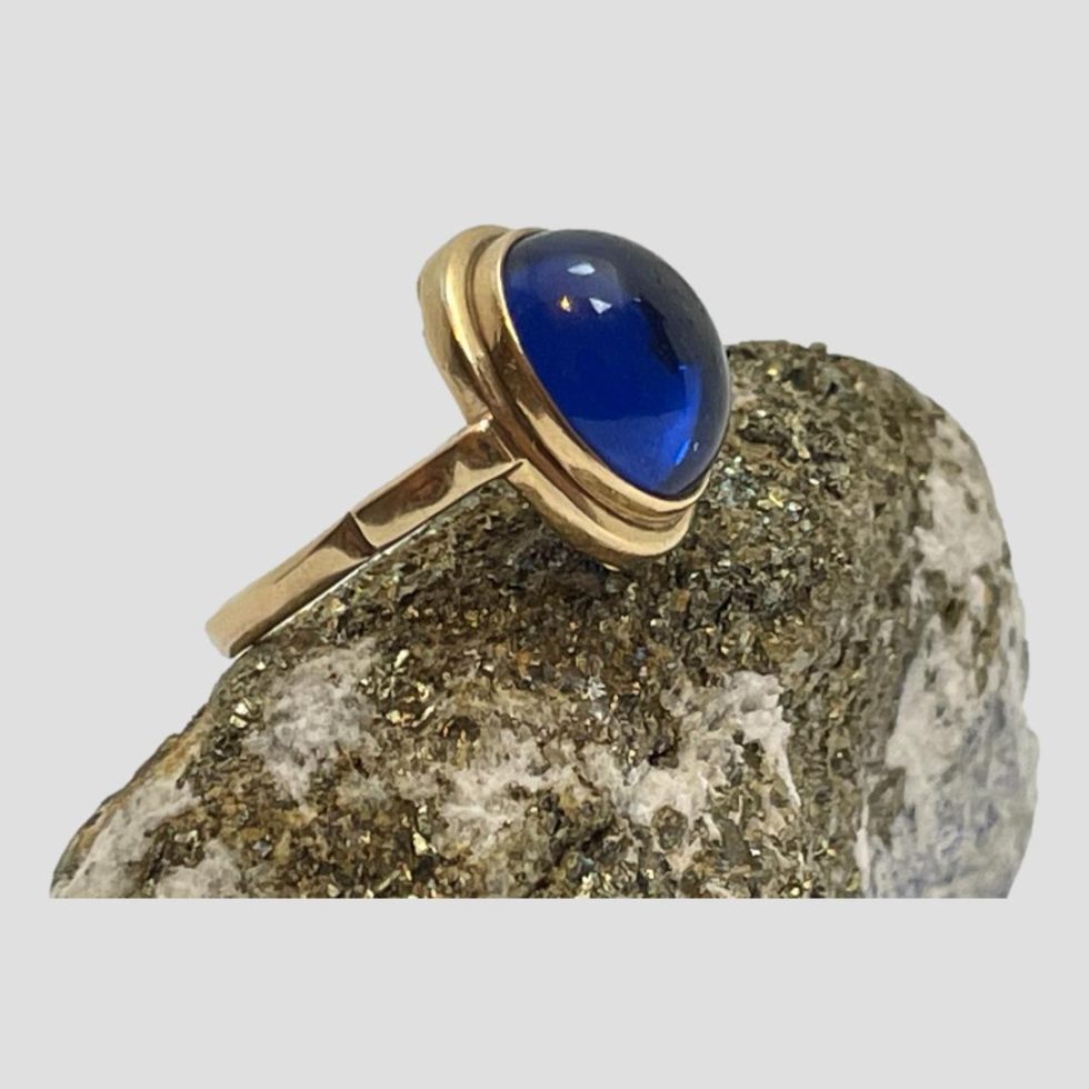 Photo of 14 karat gold blue spinel ring still displayed on top of a rock of natural lapis - gold ore side up with the ring front facing to the right.