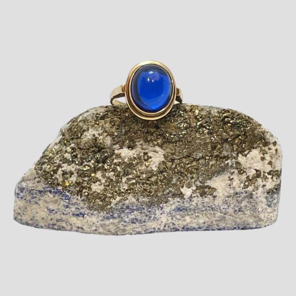 Main photo of the vintage 14 karat gold and blue spinel ring displayed on top of a small rock of natural lapis with the gold ore side on display. The blue of this spinel stone is stunning like a lagoon.