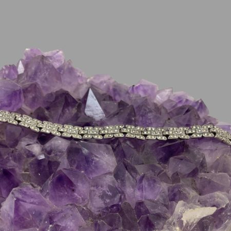 Main image of Art Deco silver bracelet displayed undone and laid out in a straight line on top of a large rock of natural amethyst crystal. The ends of the bracelet are not visible in this photo.