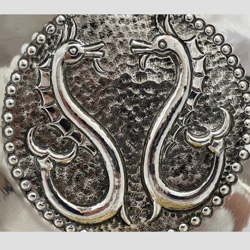 A close up photo of the centre of the sterling silver seahorse dish showing the hand chased detail to the design. The seahorses are very stylised forming an abstract S shape and almost mirroring each other as they both face inwards.