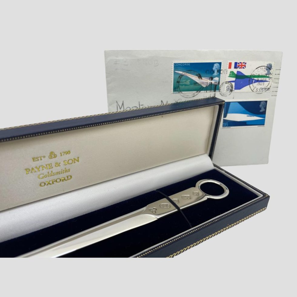 A close up of the letter opener displayed inside its case showing the gilt lettering on silk inside lid for Payne and Son. Hallmark visible on the letter opener and part of an old stamped envelope is in the background.