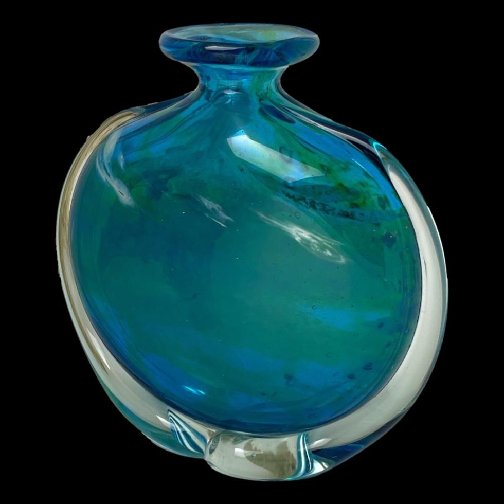 Photo of unsigned Mdina glass vase seen a little in close up with one side facing slightly to the left. The clear glass area mostly around the lower area of the vase is visible with the blue and ochre detail sits within the clear glass.