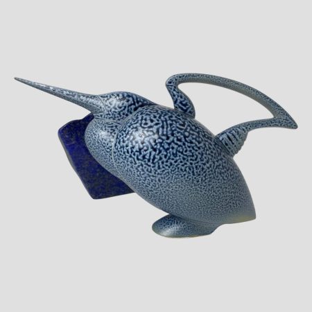 Main photo of Anthony Theakston egret jug seen from an eye level from a side angle with the bird facing direct left. Words cannot describe the beauty of this piece which spans all tastes like no other! The egret is posed in a perched position with head slightly up along with its long slender beak. The beak is the jugs spout pointed at the tip for precision pouring if brace enough to risk use. The handle is not unlike the handle of an old hob kettle and sits in perfect alignment to the beak. The whole bird is in blue speckled glaze except for the base and part of the underside of handle. There is a piece of lapis lazuli stone in the background which resembles the same colour as the birds blue specks0