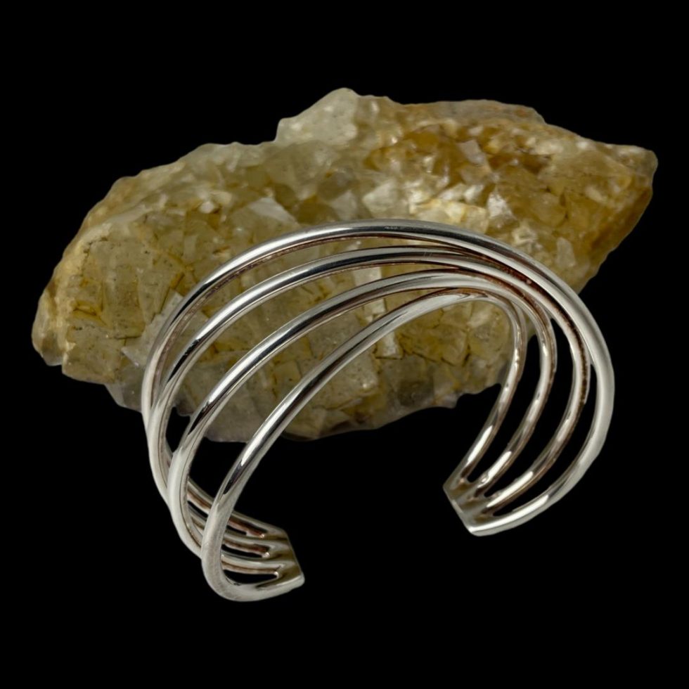 Photo of Hans Hansen silver cuff still displayed in front of a rock of natural river quartz and shot from a slightly raised angle to show the unique twist design.