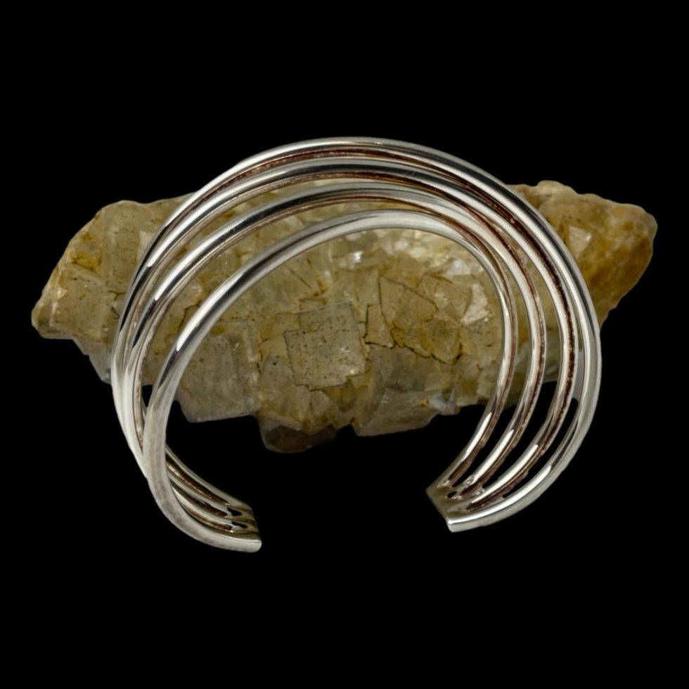 Photo of Hans Hansen silver cuff displayed in front of a rock of natural river quartz and almost from an eye level. At this angle, it is only just possible to make our the twist design at the top.