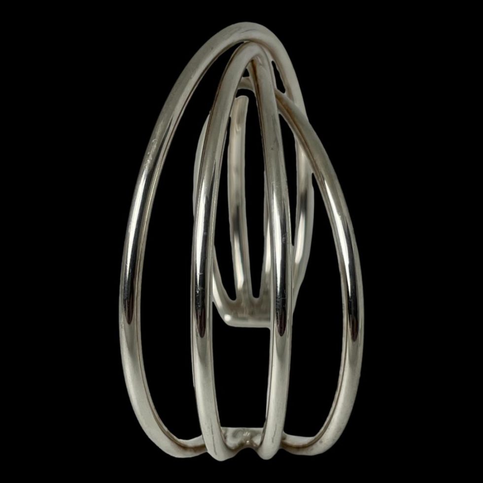 Photo of Hans Hansen silver cuff displayed upright on the cuff ends and shown from a side angle. In the foreground are 4 bands of silver which can be seen to twist at top and only part of other side visible through the gaps of bands in foreground.