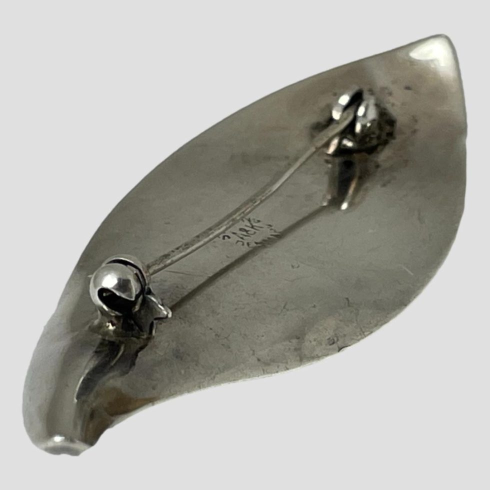 Photo of the back of Danish silver lily brooch showing pin closed. The brooch is laid diagonally across the page with one tip in top right and other in bottom left corners of photo.