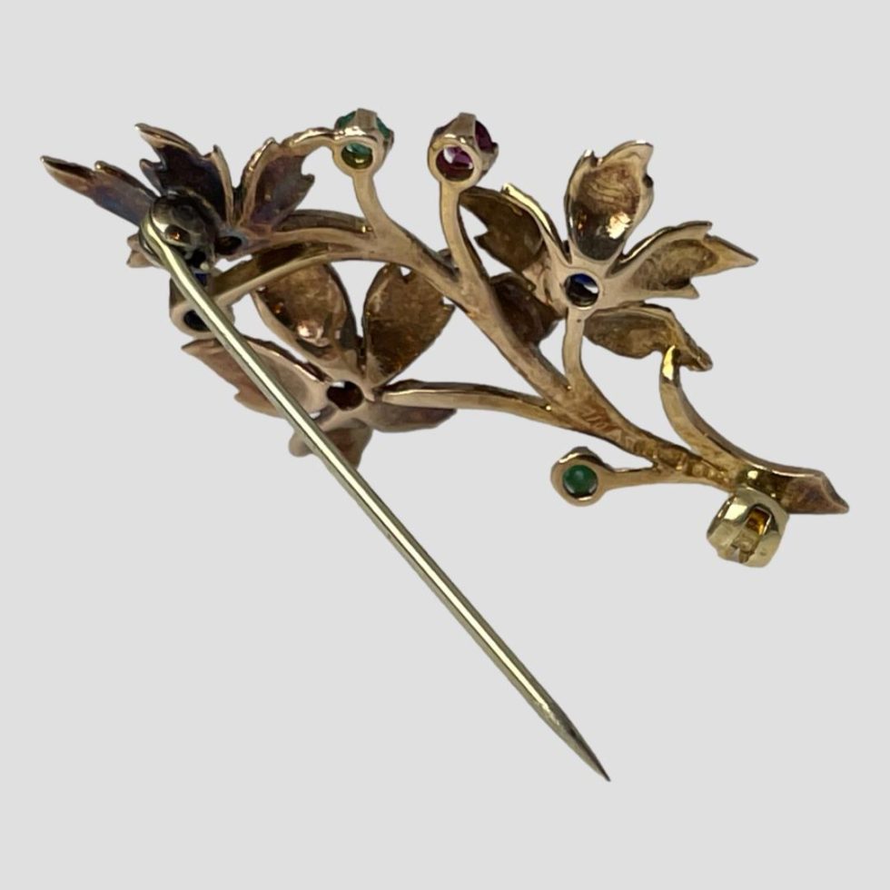 The floral spray brooch is displayed with pin open and propping itself up using pin as stand.