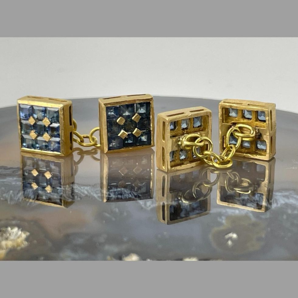 A photo of the 2 18kt gold sapphire cufflinks shown upright on the agate with one pair displaying the sapphire ends and other displaying the backs.