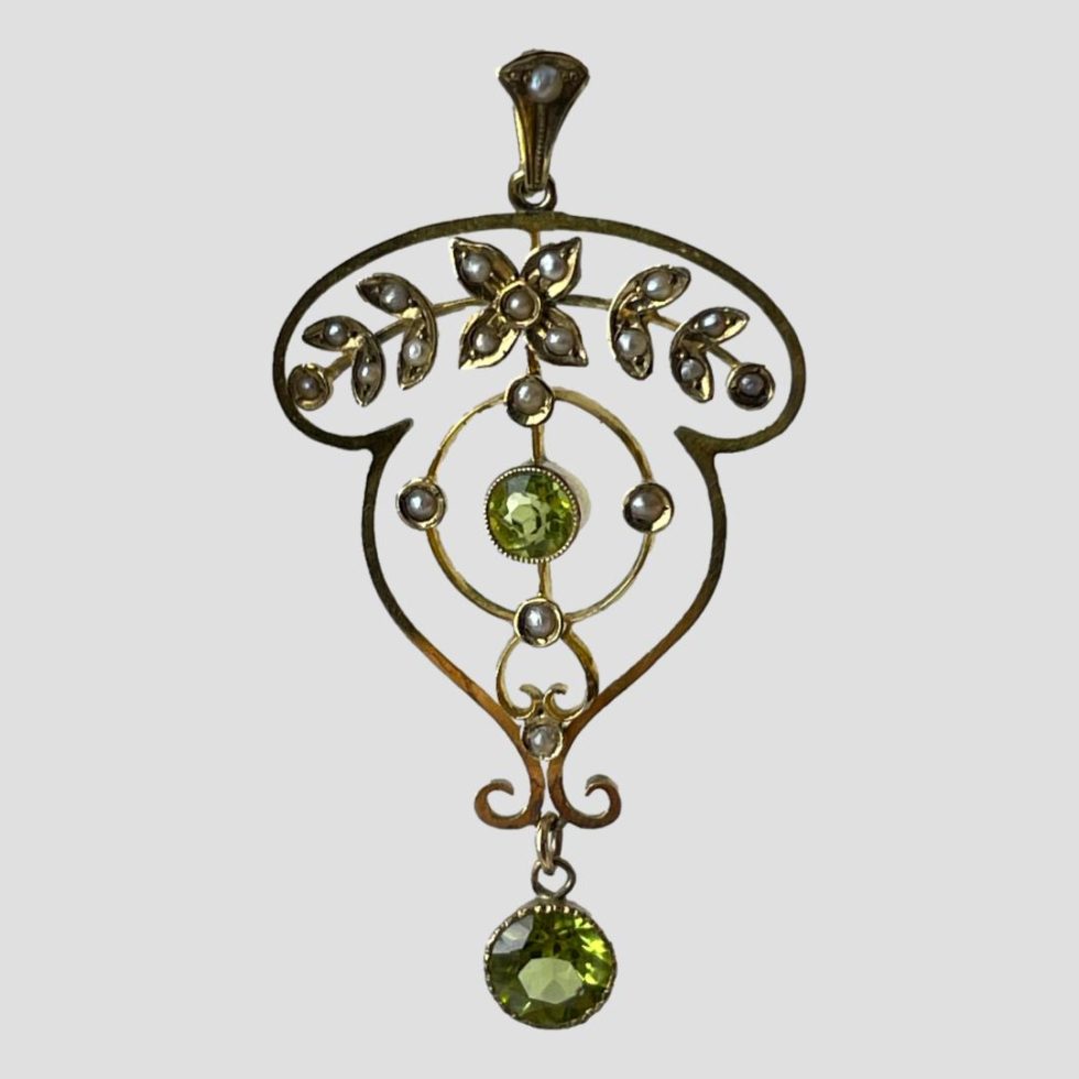 Photo of Edwardian gold peridot pendant shown hanging from invisible supports. The image has been taken from an eye level.