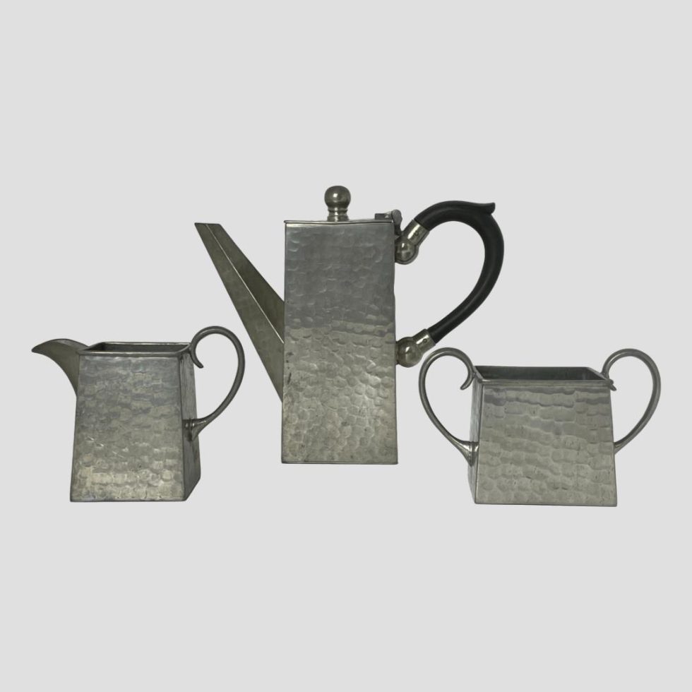 Main photo of Deco pewter coffee set shown with the 3 pieces in a row with jug to the left, coffee pot to centre and sugar bowl to right. Lovely uniform square design to each piece with pewter ear lobe handles to jug, sugar bowl and a bakelite one to coffee pot, Very aesthetically pleasing shape to each.
