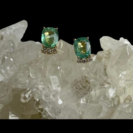 Main photo of gold emerald diamond studs displayed on top of a rock of crystal quartz with the earring fronts facing forward. The green colour of these emeralds is very unusual-more pale than regular emeralds. The diamonds are set slightly back from the emeralds but have intense sparkle.