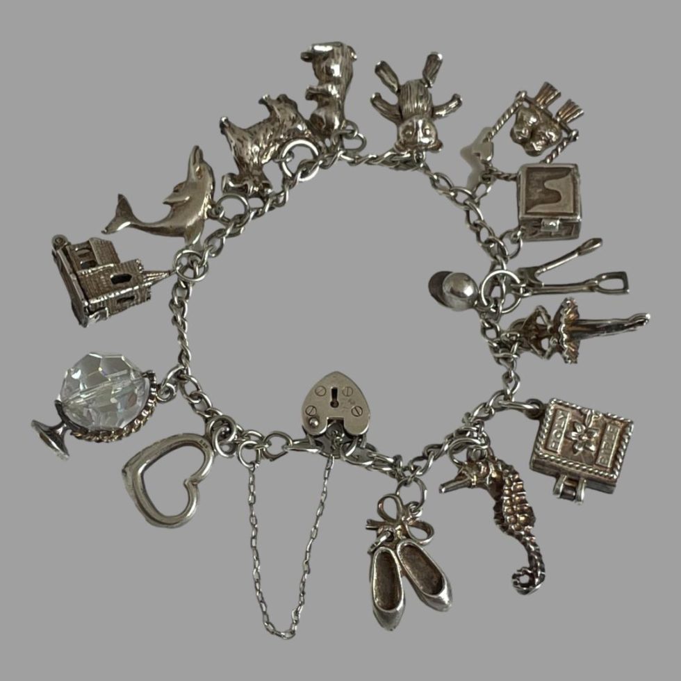 Photo of sterling silver charm bracelet displayed in a circle on a flat surface with each charm fanned out around the bracelet chain. The heart clasp is the only item inside the chain bracelet.