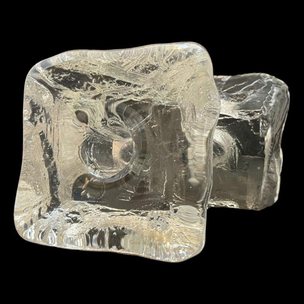 Photo of Swedish 'ice' candle holders seen propped up on their side with one in foreground showing the top with candle slot and other behind & protruding to the right shows the base. The resemblance to ice is really amazing. The original sticker for designer Göte Augustsson is visible on the bottom right corner of the one in front.