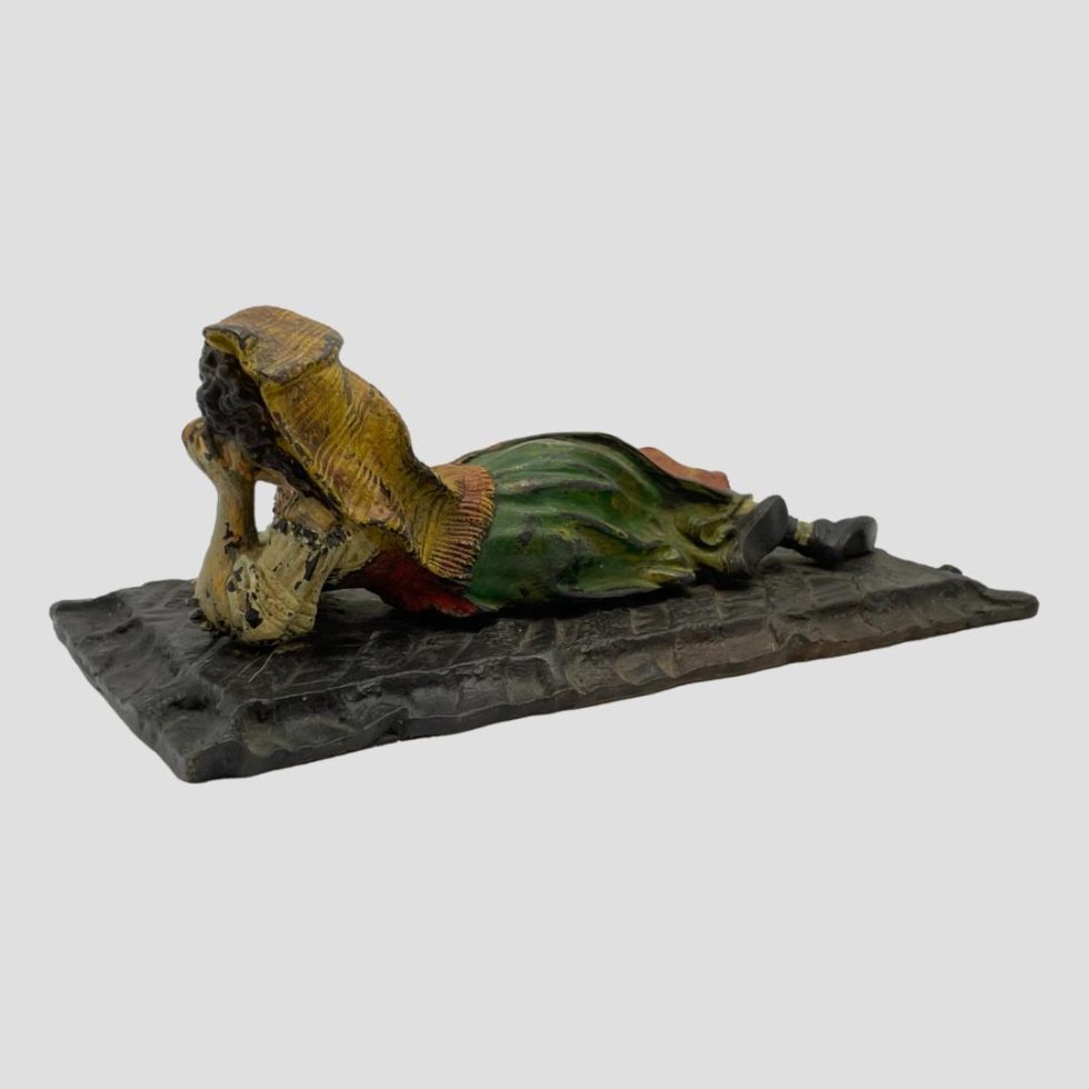 Photo of vintage bronze Bedouin girl displayed from the back. The angle is set at a slight diagonal so her feet are faced toward top right corner and upper torso and head towards bottom left.