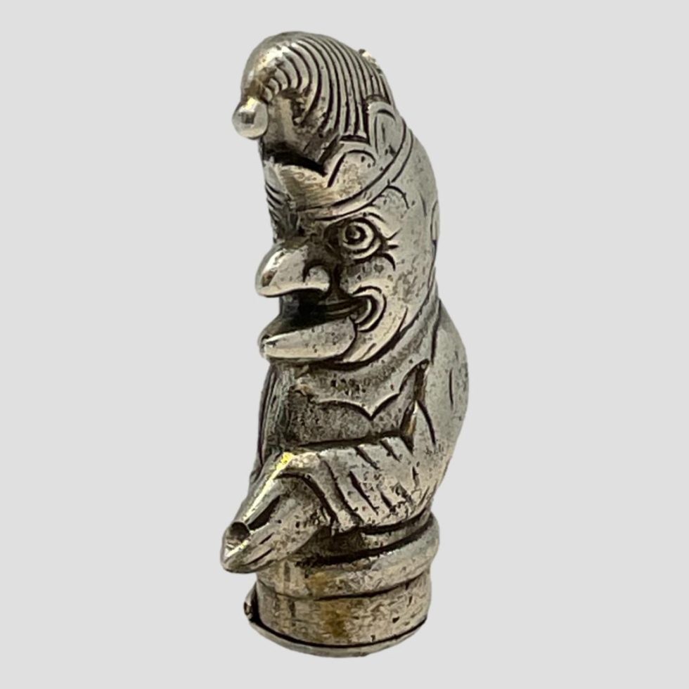 Photo of vintage silver Punch vesta seen from a diagonal angle with Mr Punch facing towards the bottom left corner. His facial expression is bordering on sinister at this angle!