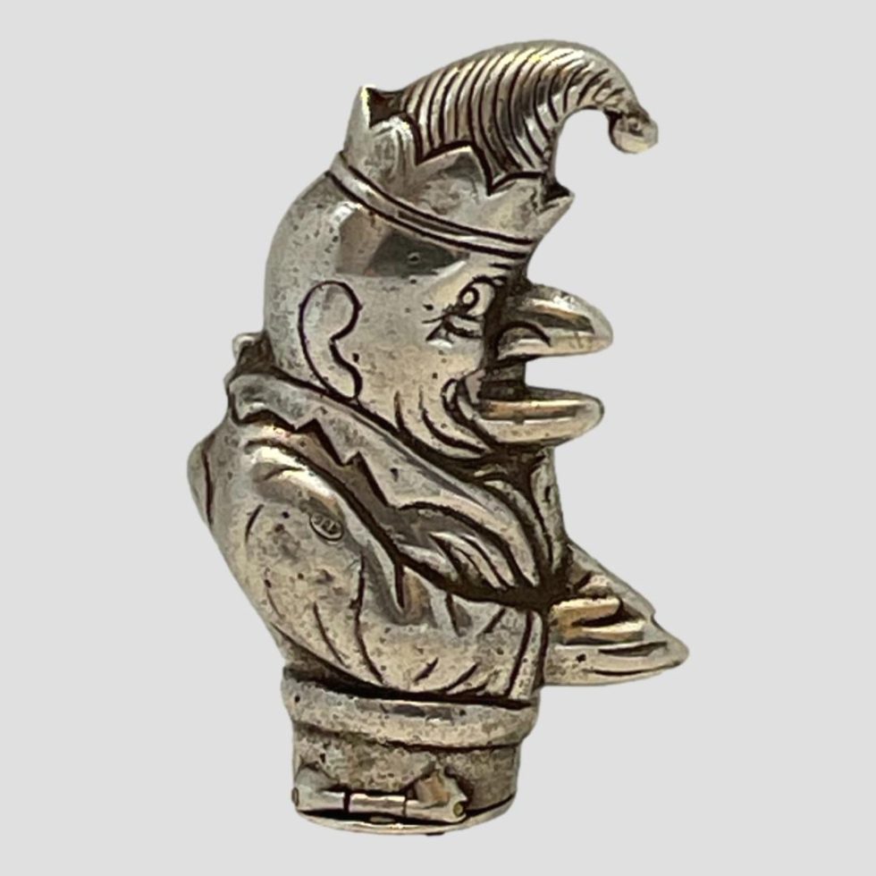 Main photo of vintage silver Punch vesta seen from a side angle with Mr Punch facing right. The 925 hallmark is just visible to top of his arm here. He is wearing a floppy hat with a bell on top and has his hands together in front of him. His mouth is open and his lips resembles a birds beak.