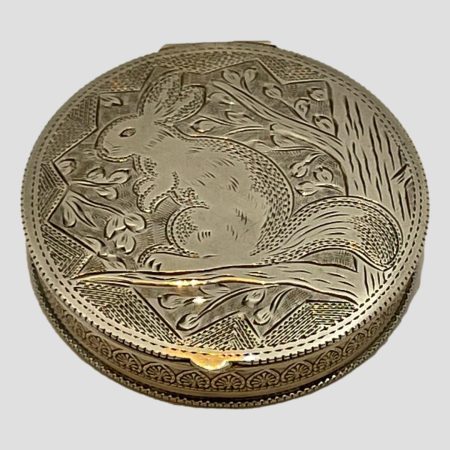 Main photo of 1930s Austrian silver compact shown laid on a flat surface and looking diagonally down at the top of lid. The European squirrels are red and have longer ears than grey squirrels. This squirrel is sitting on a branch up a tree and seen in profile in typical squirrel high alert pose.