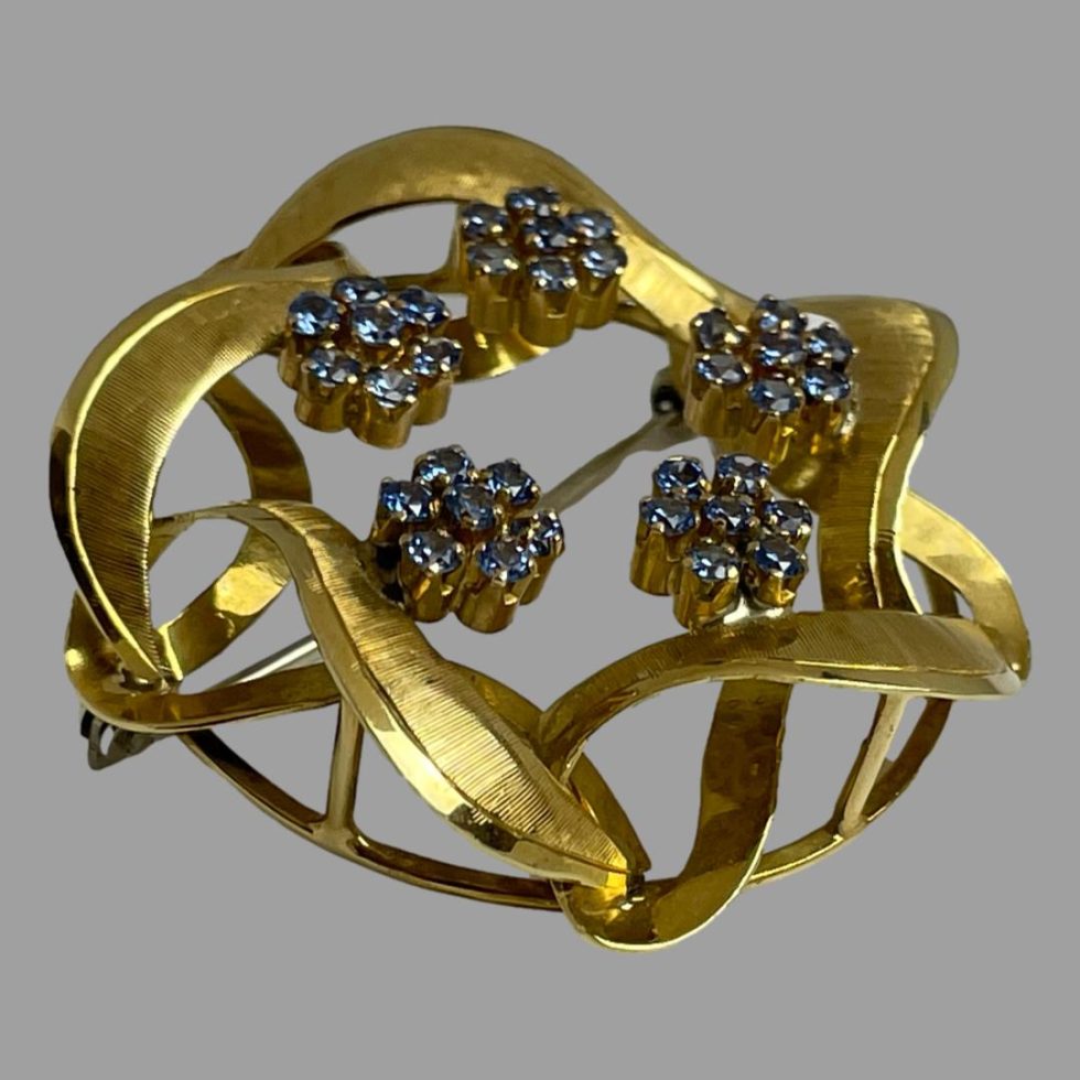 Photo of gold blue topaz brooch displayed on a flat surface and shown from a side angle with brooch front tilted up towards the top right corner or picture.
