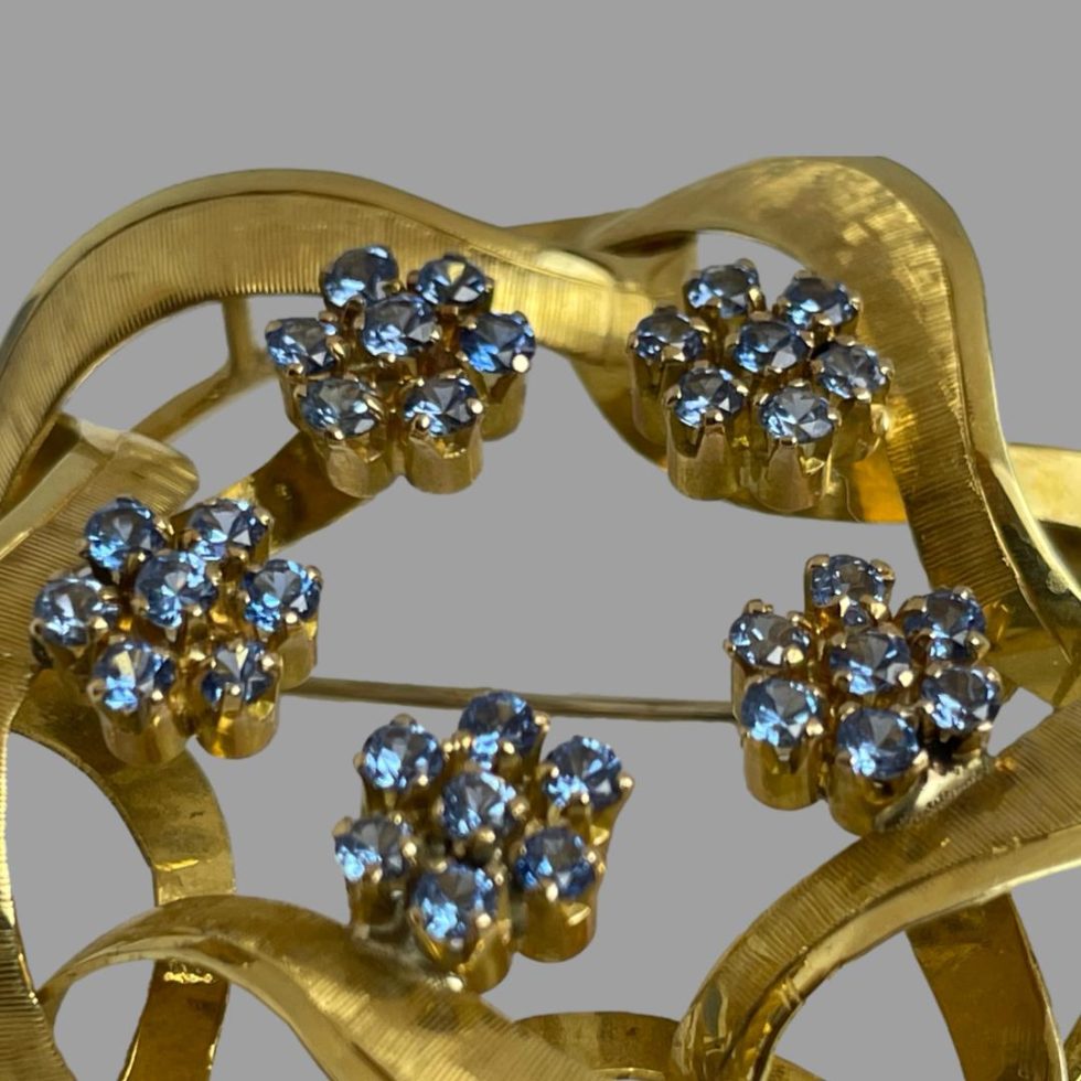 A close up photo of the gold blue topaz brooch focusing on the blue topaz flower heads to the centre of the wreath.