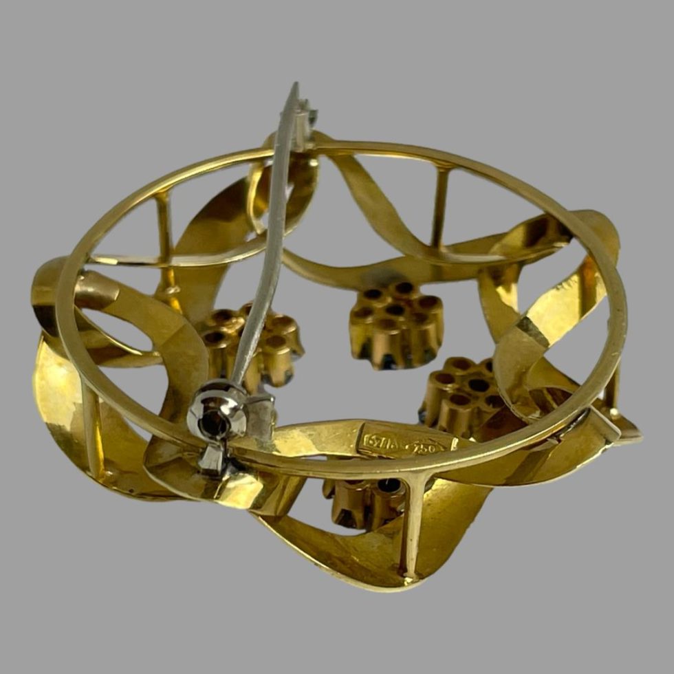 Photo of the back of gold blue topaz brooch shown facedown on a flat surface . The pin is shown closed and is of silver metal as are the clasp and hinge.